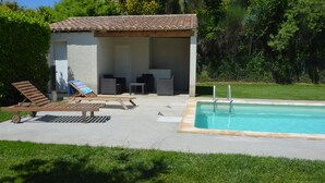 Zona junto a la piscina con un espacio de descanso cubierto, sillas de reposo y una alberca.