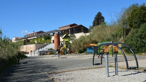 Un parque infantil con tobogán y columpios, un edificio de techo rojo y una escalera que lleva al edificio.