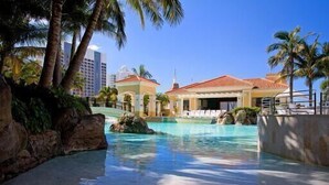 A resort with a pool, palm trees, and a building with a red roof. - Chevron – 3 Bed Executive Sub Penthouse Ocean (Surfers Paradise)