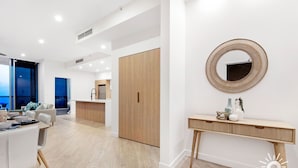 A modern living room with a dining area, a wooden wardrobe, and a round mirror on the wall. - Chevron – 3 Bed Executive Sub Penthouse Ocean (Surfers Paradise)
