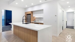 A modern kitchen with a central island, white cabinetry, and a view to the outside. - Chevron – 3 Bed Executive Sub Penthouse Ocean (Surfers Paradise)