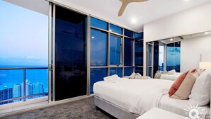 A modern hotel room with a large sliding glass door, a bed, a bedside table, and a city view. - Chevron – 3 Bed Executive Sub Penthouse Ocean (Surfers Paradise)
