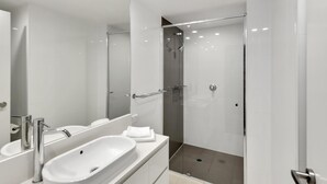 A modern bathroom with a large mirror, a white sink, and a glass-enclosed shower. - H'Residences – 2 Bed City View — Q Stay (Surfers Paradise)