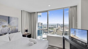A hotel room with a large bed, a desk with a TV, a city view, and a painting on the wall. - H'Residences – 2 Bed City View — Q Stay (Surfers Paradise)