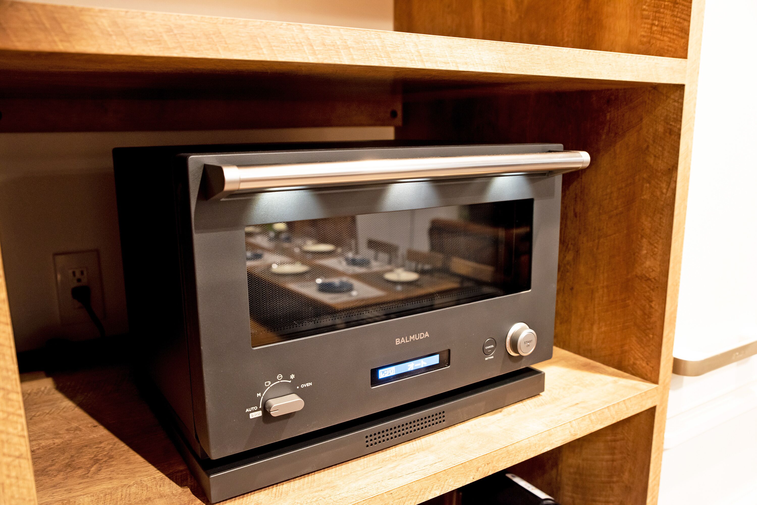 A kitchen with a built-in oven and microwave, a wooden shelf above, and a power outlet on the wall.