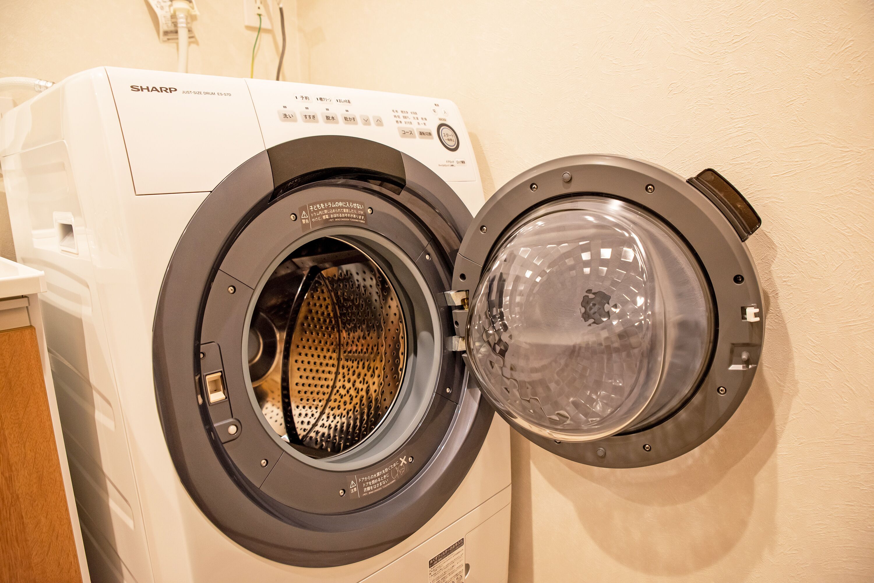 A front-loading washing machine with a transparent door, control panel, and safety labels.