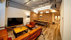 A modern living room with a large flat-screen TV, leather sofas, a wooden coffee table, and a dining area with a long table and chairs. - American Vintage Suite (Tokyo)