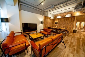A modern living room with leather sofas, a wooden coffee table, a TV, and a bar area with wooden paneling and pendant lighting. - American Vintage Suite (Tokyo)