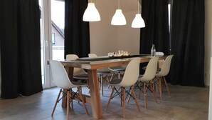 Un comedor con mesa de madera, sillas blancas y lámparas colgantes.