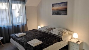 Un dormitorio con cama, mesita de noche, lámpara, un cuadro y ventana con cortinas.