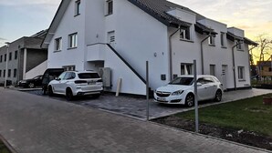 Un edificio moderno de dos pisos con techo inclinado, una entrada para coches y dos automóviles estacionados.