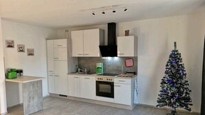 Una cocina moderna con armarios blancos, horno empotrado y una pequeña isla. Se ve un árbol de Navidad en una esquina.