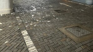 A paved courtyard with a metal manhole cover, a low wall, and a building in the background with string lights. - Premier Executive Apartment - The Ivy, East Legon (East Legon)
