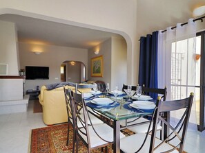 A dining area with a glass table, chairs, and a sofa in the background.
