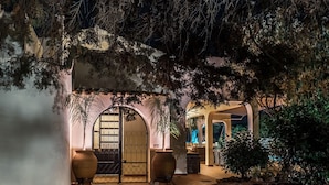 An outdoor area with a wooden bench, a large potted plant, and a gate leading to a building. - Quinta Pequena is a traditional,  3 bedroom Apartment/Villa near Vale Do Lobo. (Quinta Pequena Almancil,)