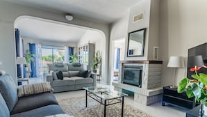A living room with a fireplace, a sofa, a coffee table, and a view through an archway to a balcony. - Quinta Pequena is a traditional,  3 bedroom Apartment/Villa near Vale Do Lobo. (Quinta Pequena Almancil,)
