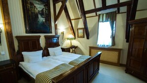 Une chambre traditionnelle avec un grand lit, des poutres en bois, un tableau au mur et une fenêtre avec des rideaux.