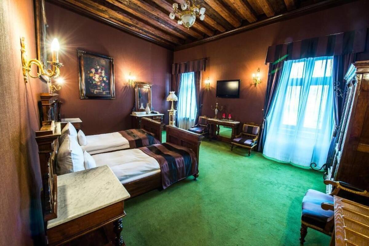 A hotel room with two beds, a desk, a chair, a television, and a chandelier.