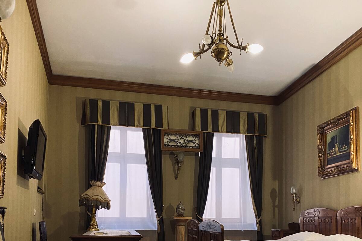 A bedroom with a bed, a desk, a chair, a lamp, and a chandelier.