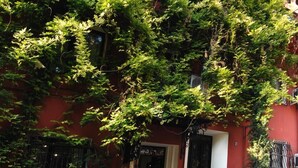 Un edifici vermell amb una porta blanca, envoltat de plantes en testos i una estàtua d'un cigne blanc.