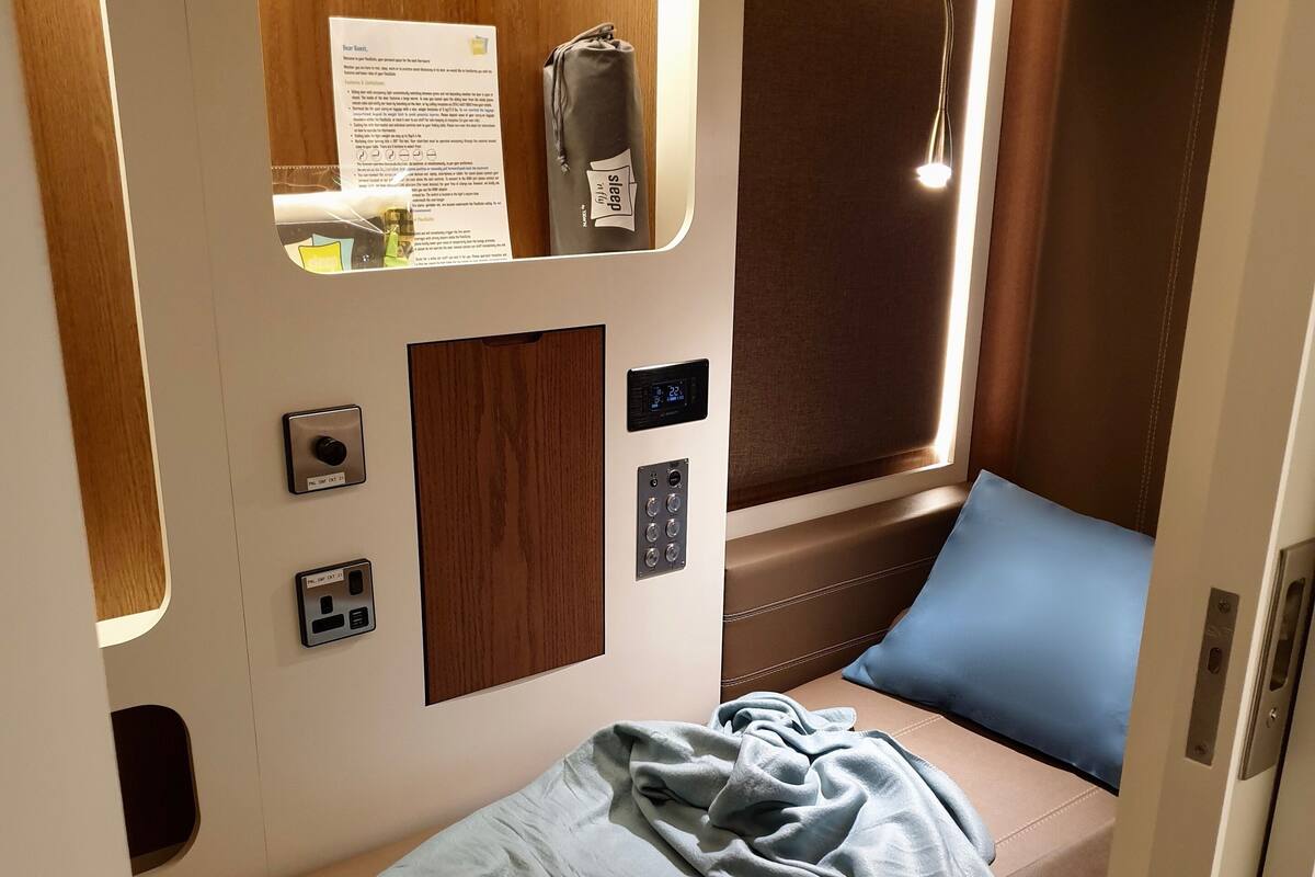 Ein kompakter, gut beleuchteter Raum mit einem kleinen Bett, einer Bedienkonsole und einem Fenster mit Vorhängen.