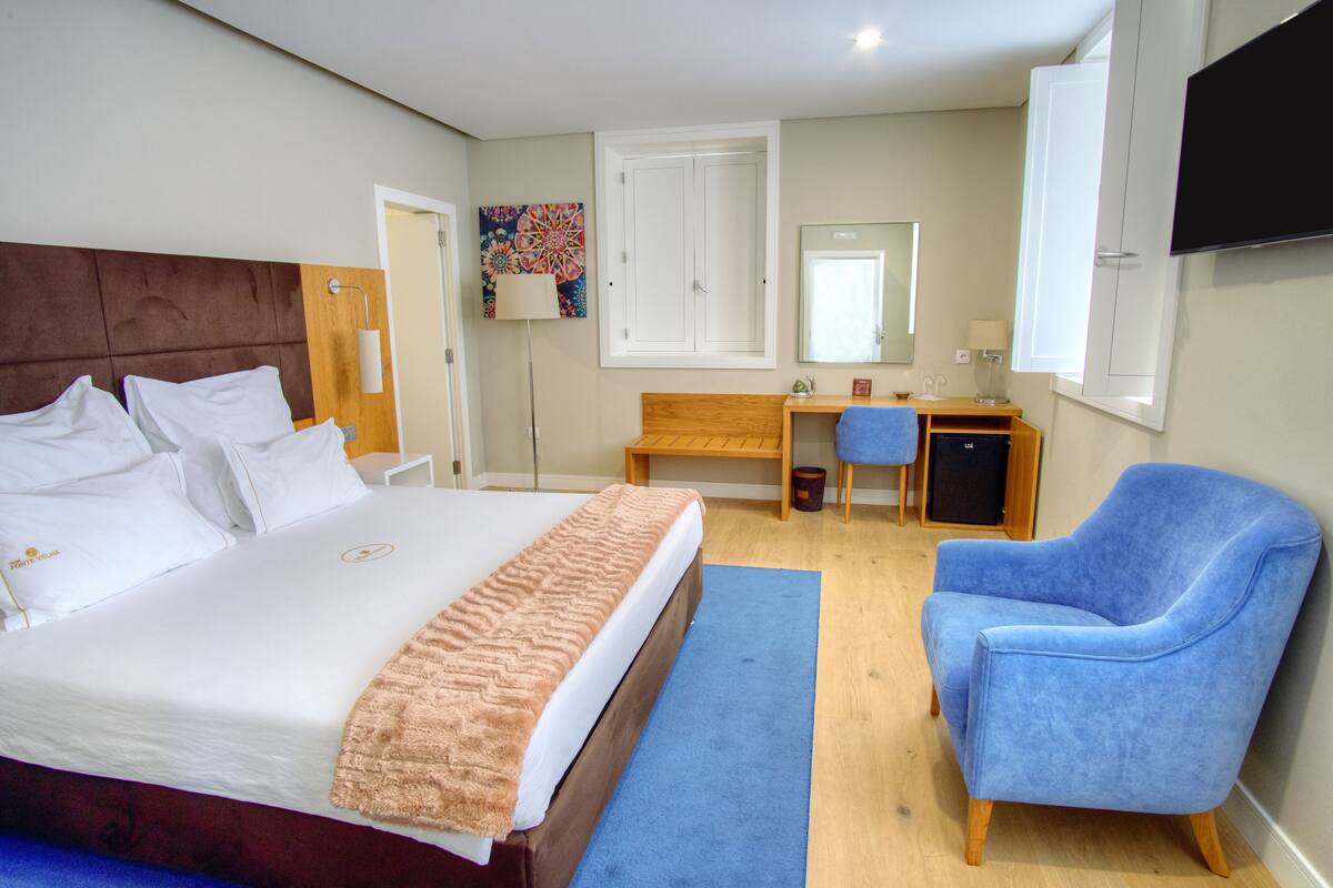 A hotel room with a large bed, a desk, a chair, and a TV on the wall.