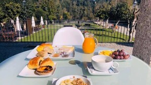 A table set outdoors with a variety of breakfast items including croissants, a bowl of fruit, and a jug of orange juice. - Hotel Fonte Velha (Ponte da Barca)