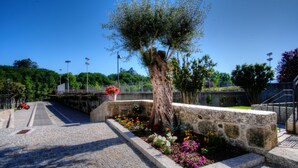A stone pathway leading to a stone bench with a tree and flower bed. - Hotel Fonte Velha (Ponte da Barca)