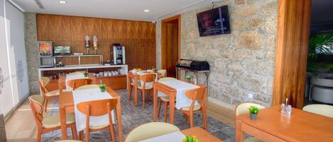 A hotel dining area with wooden tables and chairs, a stone wall, and a television mounted on the wall.