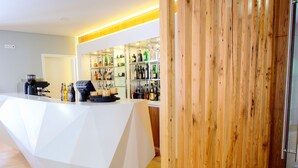 A modern reception area with a geometric white counter, wooden paneling, and a glass door leading to a bar area with shelves of bottles. - Hotel Fonte Velha (Ponte da Barca)