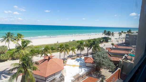A beach view with a clear sky, palm trees, and a building with a red roof. - 661 Partial Ocean View Hollywood Beach (Hollywood)