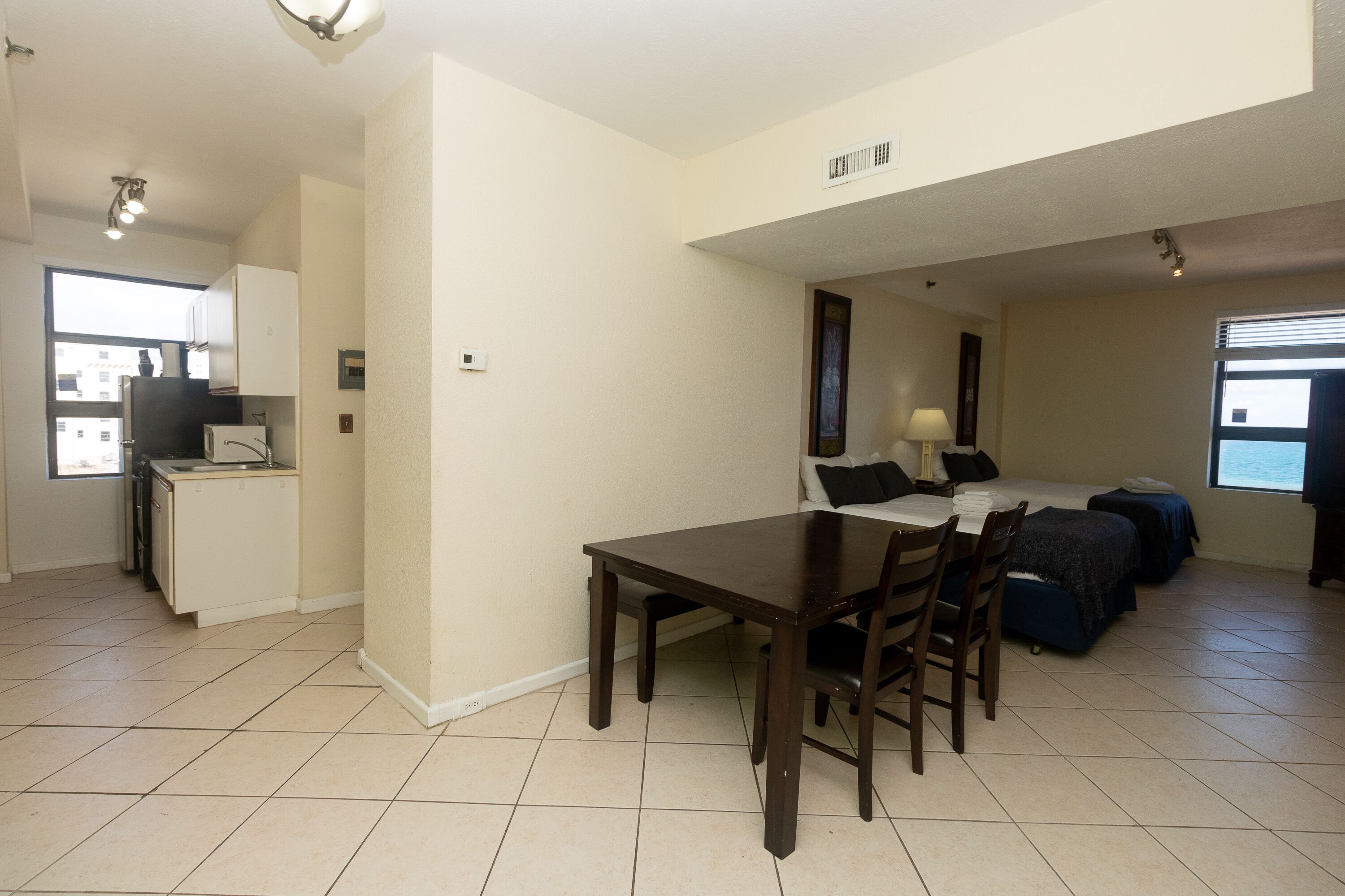 A compact living space with a dining table, chairs, a kitchenette, a bed, and a window.