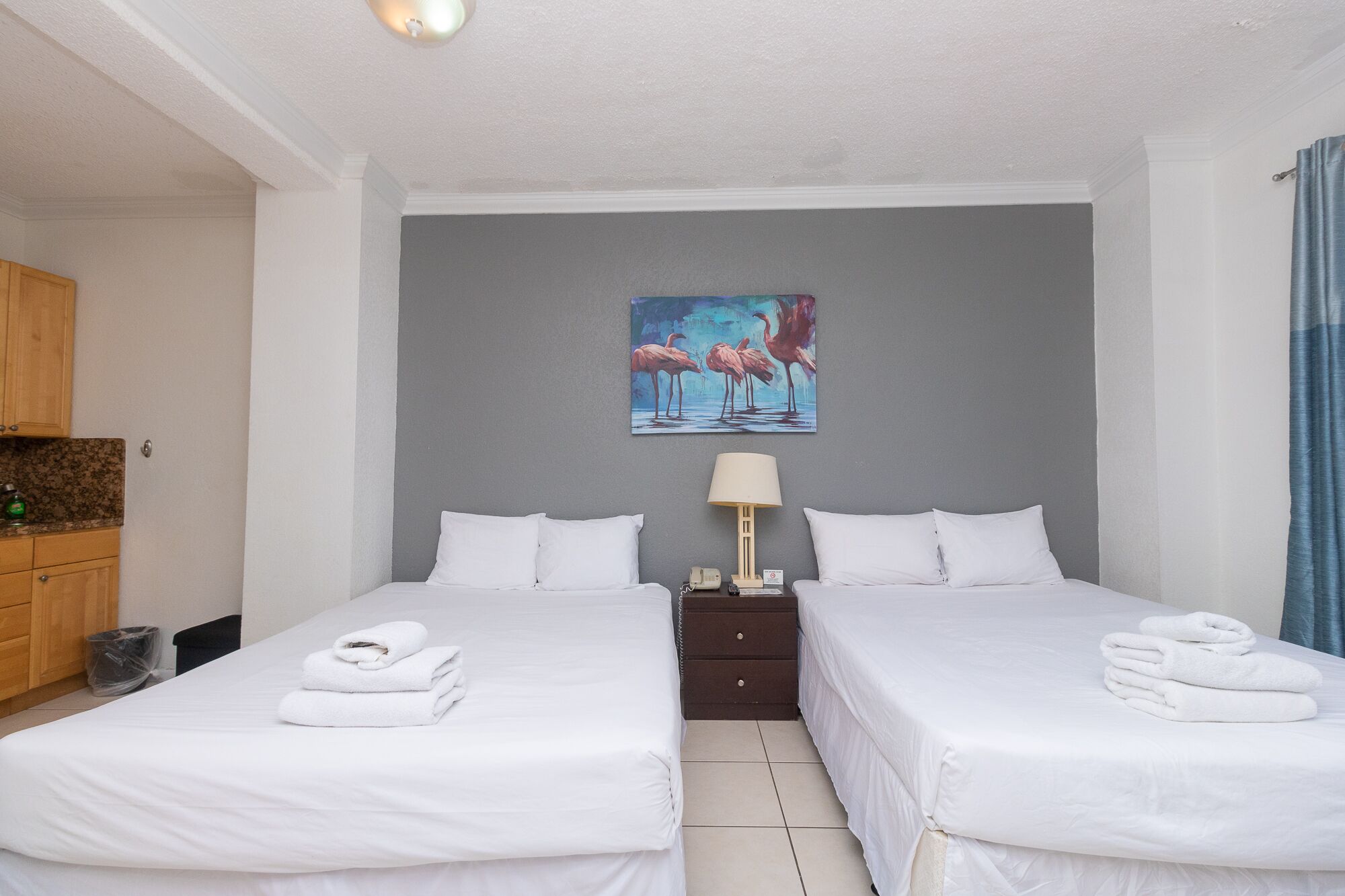 Een hotelkamer met twee bedden, een flamingo schilderij aan de muur, een lamp en een houten kast.