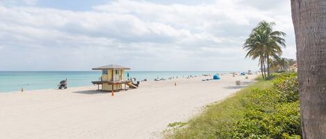 A beach with a lifeguard tower, palm trees, and a clear sky.