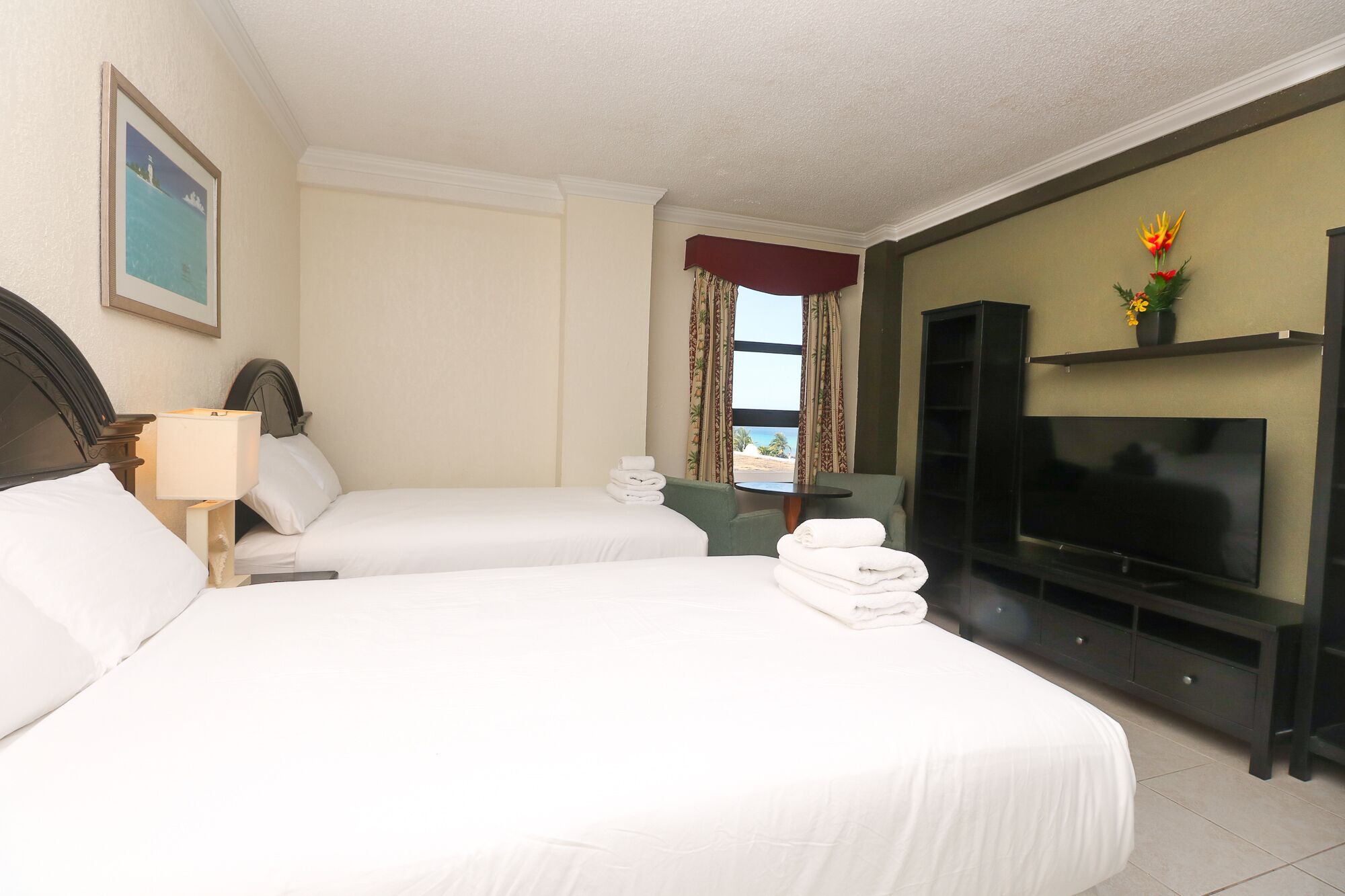 A hotel room with two beds, a TV, a small table, and a window with curtains.