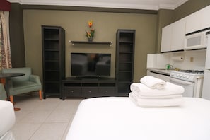 A hotel room with a bed, a TV, a kitchenette, and a seating area with a table and chair.