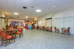 A spacious indoor dining area with multiple tables and chairs, a Coca-Cola refrigerator, and a vending machine.
