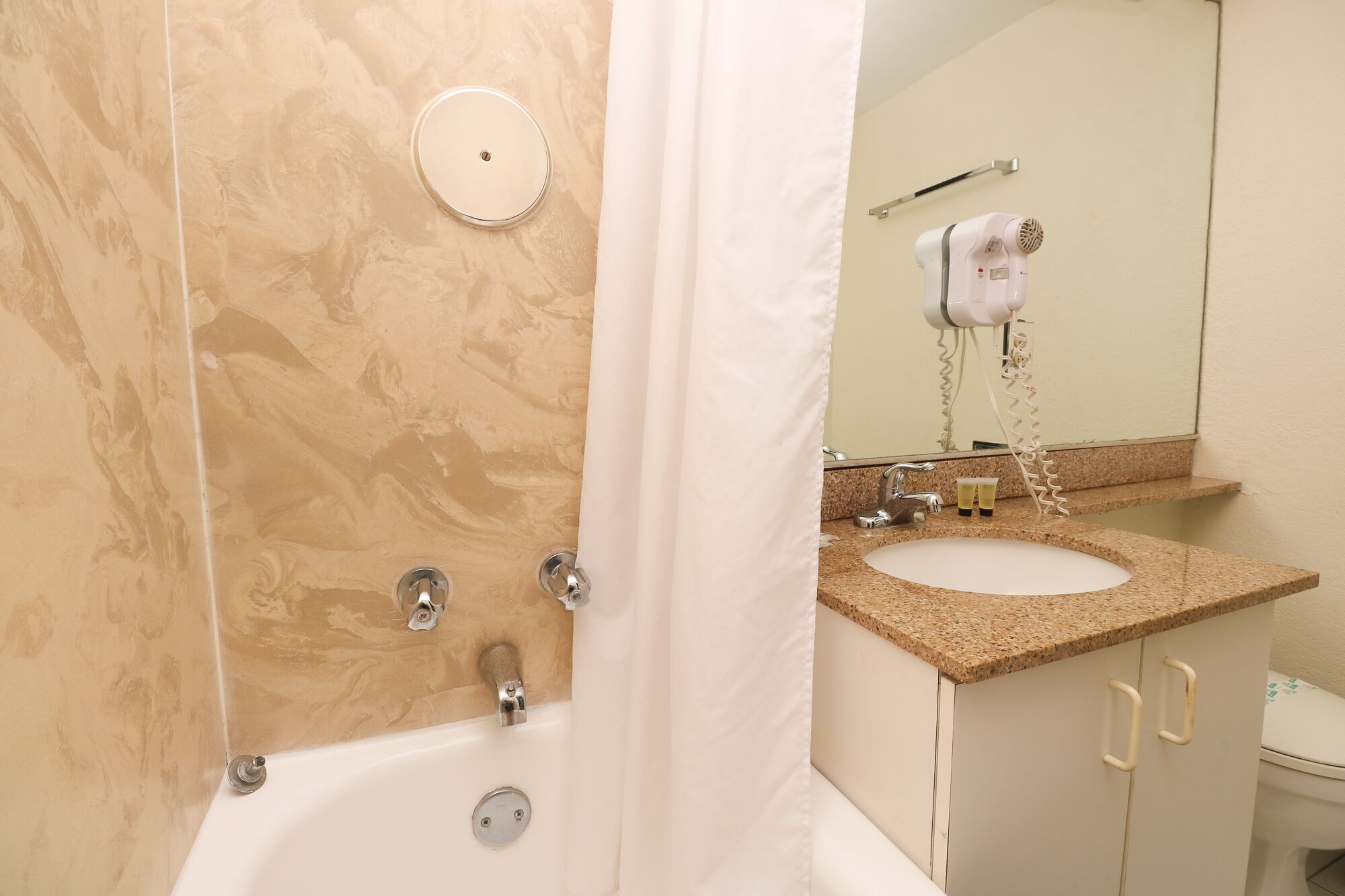 A bathroom with a bathtub, two sinks, a hairdryer, and a mirror.
