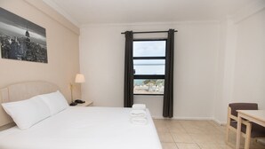 A hotel room with a bed, a nightstand with a lamp, a desk, and a window with curtains. - 436 Ocean View Studio (Hollywood)