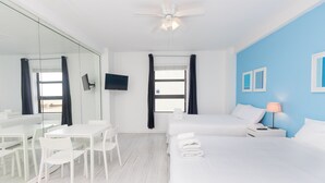 Een hotelkamer met een bed, bureau, stoelen, televisie en plafondventilator.