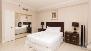 Une chambre d’hôtel avec un grand lit, deux tables de chevet avec des lampes, un téléviseur à écran plat, un miroir et une porte.