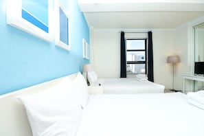 A hotel room with two beds, a window with curtains, a desk with a lamp, and a TV on a stand.