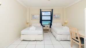 Een hotelkamer met twee bedden, een bureau en uitzicht op zee.