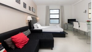 A modern hotel room with a bed, a black sofa with red and grey cushions, a desk with a TV, and a large window with a view of the sea. - 774 Ocean View Hollywood Beach (Hollywood)