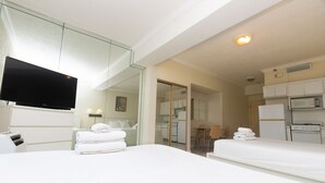 Hotelkamer met twee bedden, een televisie, een kitchenette en een badkamer, zichtbaar door een geopende deur.
