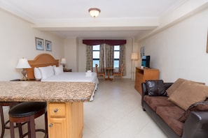 A hotel room with a bed, a desk with a chair, a sofa, a TV, and a view of the sea through the windows. - 746 Ocean View Hollywood Beach Resort (Hollywood)