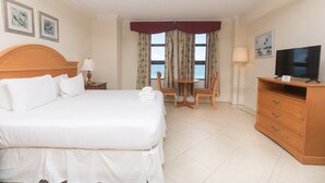 A hotel room with a bed, a TV, a desk with two chairs, a lamp, and curtains with a view of the sea. - 746 Ocean View Hollywood Beach Resort (Hollywood)