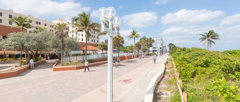 Une promenade pavée bordée de palmiers, une piste cyclable et des bâtiments en arrière-plan.