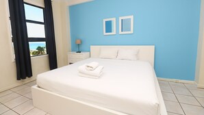 A hotel room with a bed, a nightstand, a lamp, and a view of the ocean.