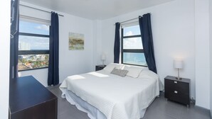 A modern bedroom with a large bed, two bedside tables, a desk, and a view of the sea. - 701 Ocean View Hollywood Beach (Hollywood)